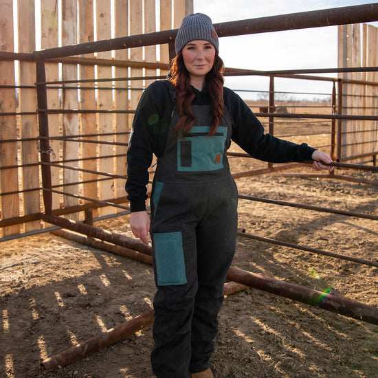 Person wearing a black and teal overalls standing inside a wooden pen.