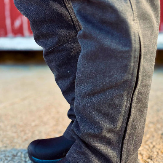 Person wearing dark blue winter boots and black overalls on a textured surface.