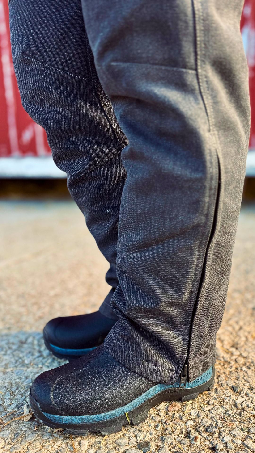 Person wearing dark blue winter boots and black overalls on a textured surface.