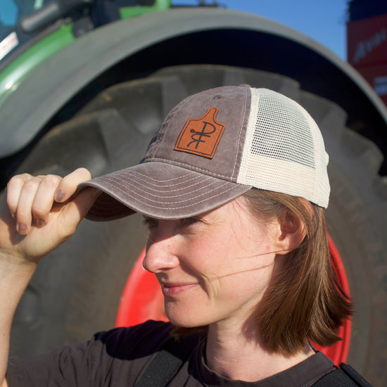 Person wearing a cap with a logo in front of a tractor