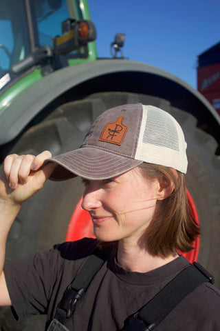 Person wearing a cap with a logo in front of a tractor