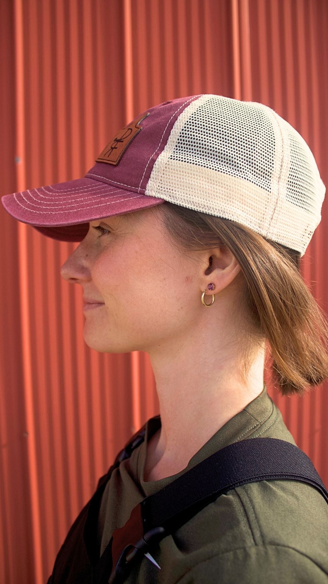 Person wearing a maroon and beige cap against a red corrugated metal background