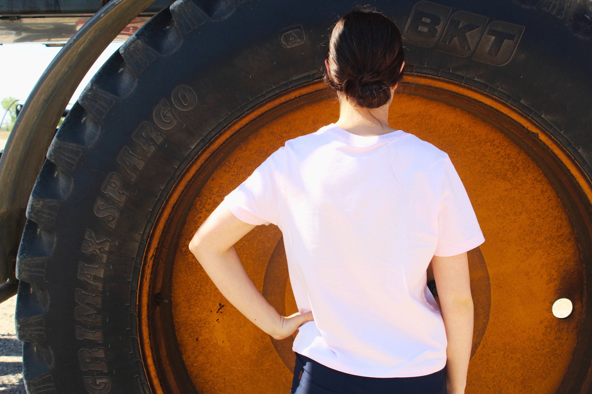 Person in a pink shirt standing in front of a large tire.