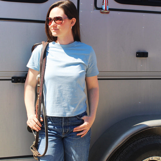 A woman standing beside a vehicle wearing a blue cotton tee and blue jeans