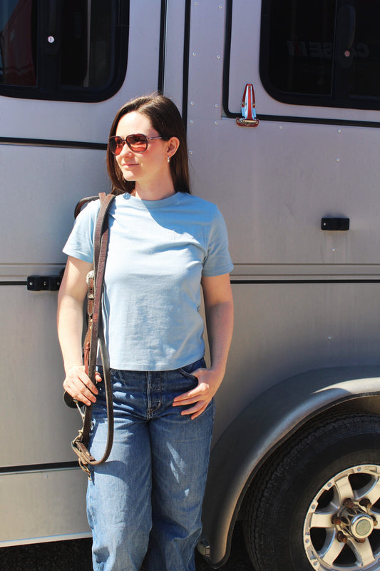 A woman standing beside a vehicle wearing a blue cotton tee and blue jeans