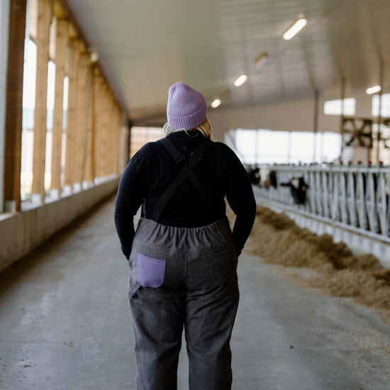 Person wearing grey overalls with purple pocket and toque in barn setting 