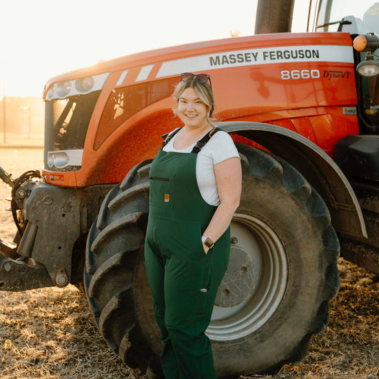 Person in green overalls standing next to a Massey Ferguson tractor on a farm.