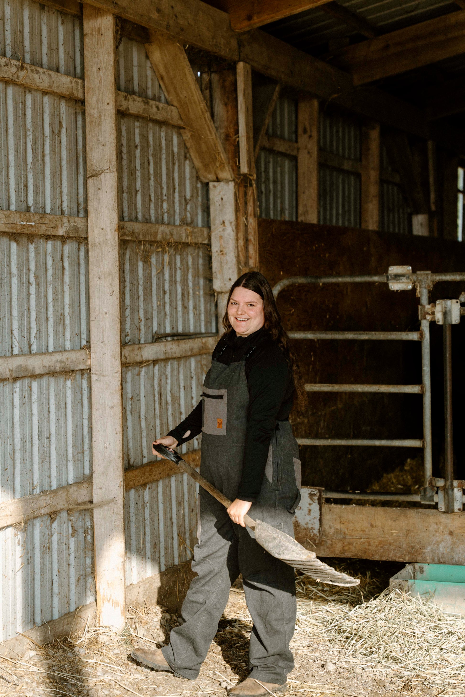 Person holding a broom inside a barn with wooden walls and hay on the floor.