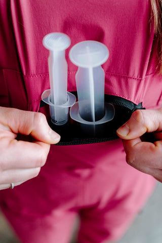 Person holding a black case with two clear plastic items inside, against a pink background.