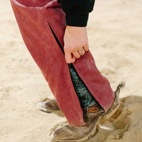 Person wearing pink overalls and brown boots stepping into sand