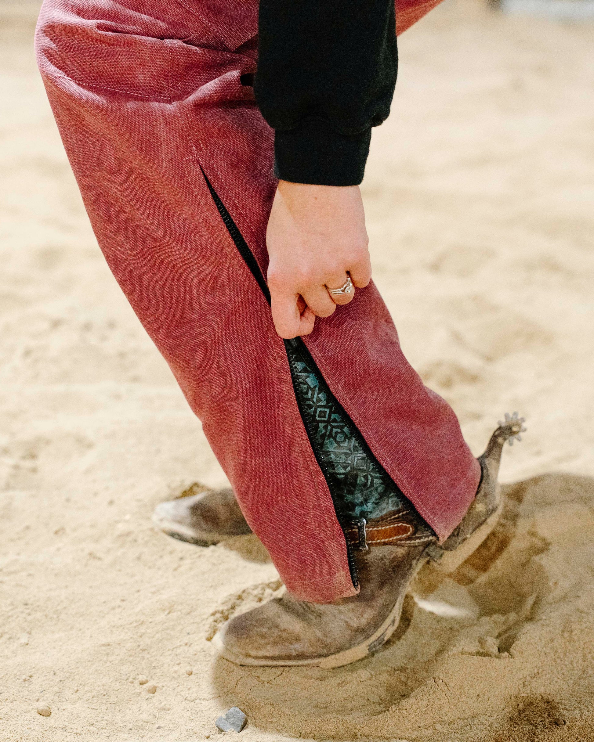 Person wearing pink overalls and brown boots stepping into sand