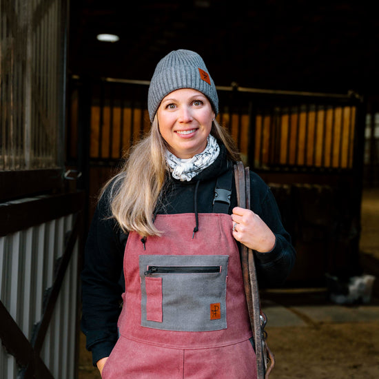 Person wearing a pink overalls and gray knit hat in a stable