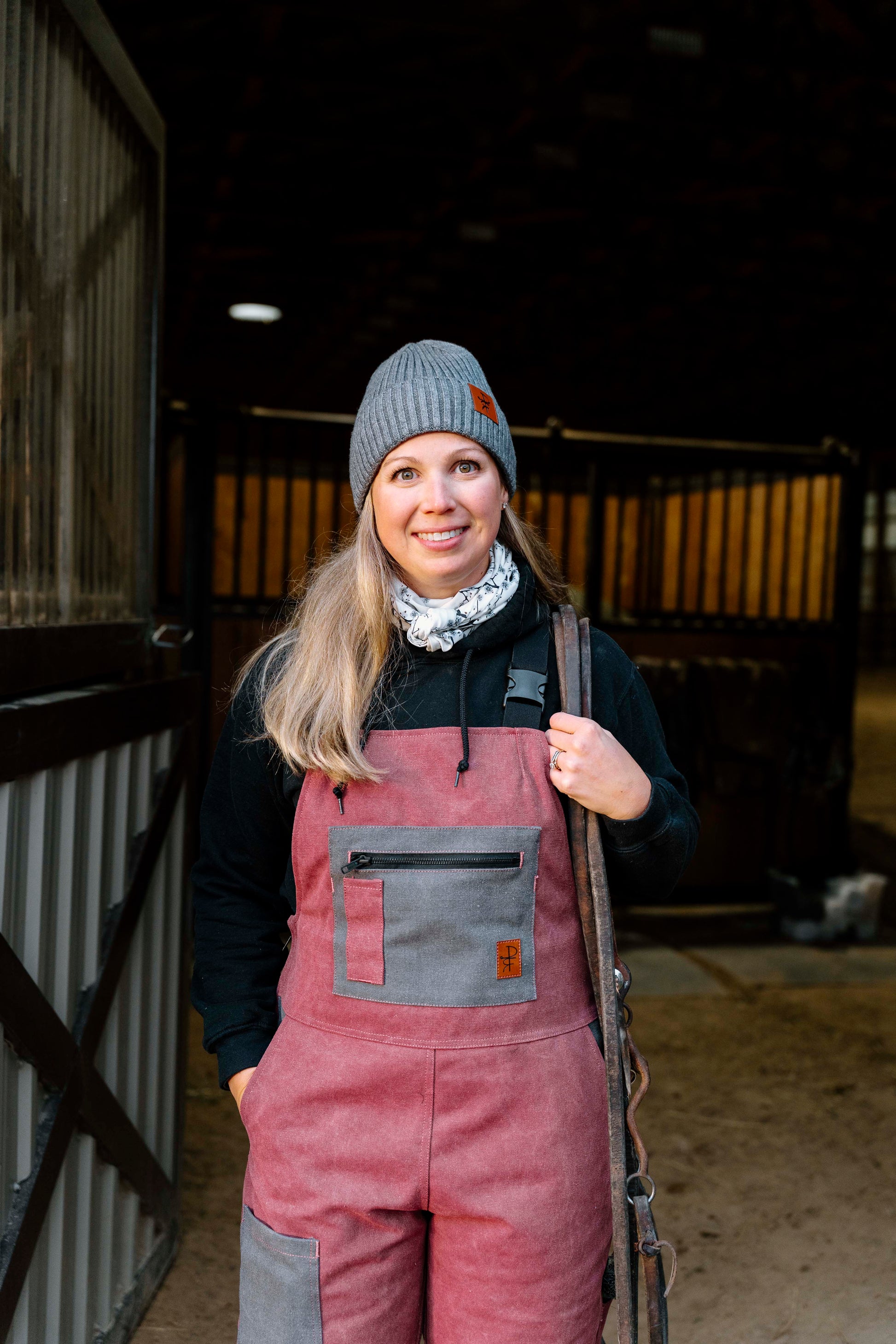 Person wearing a pink overalls and gray knit hat in a stable