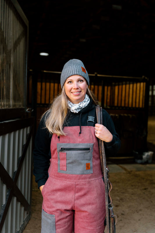 Person wearing a pink overalls and gray knit hat in a stable