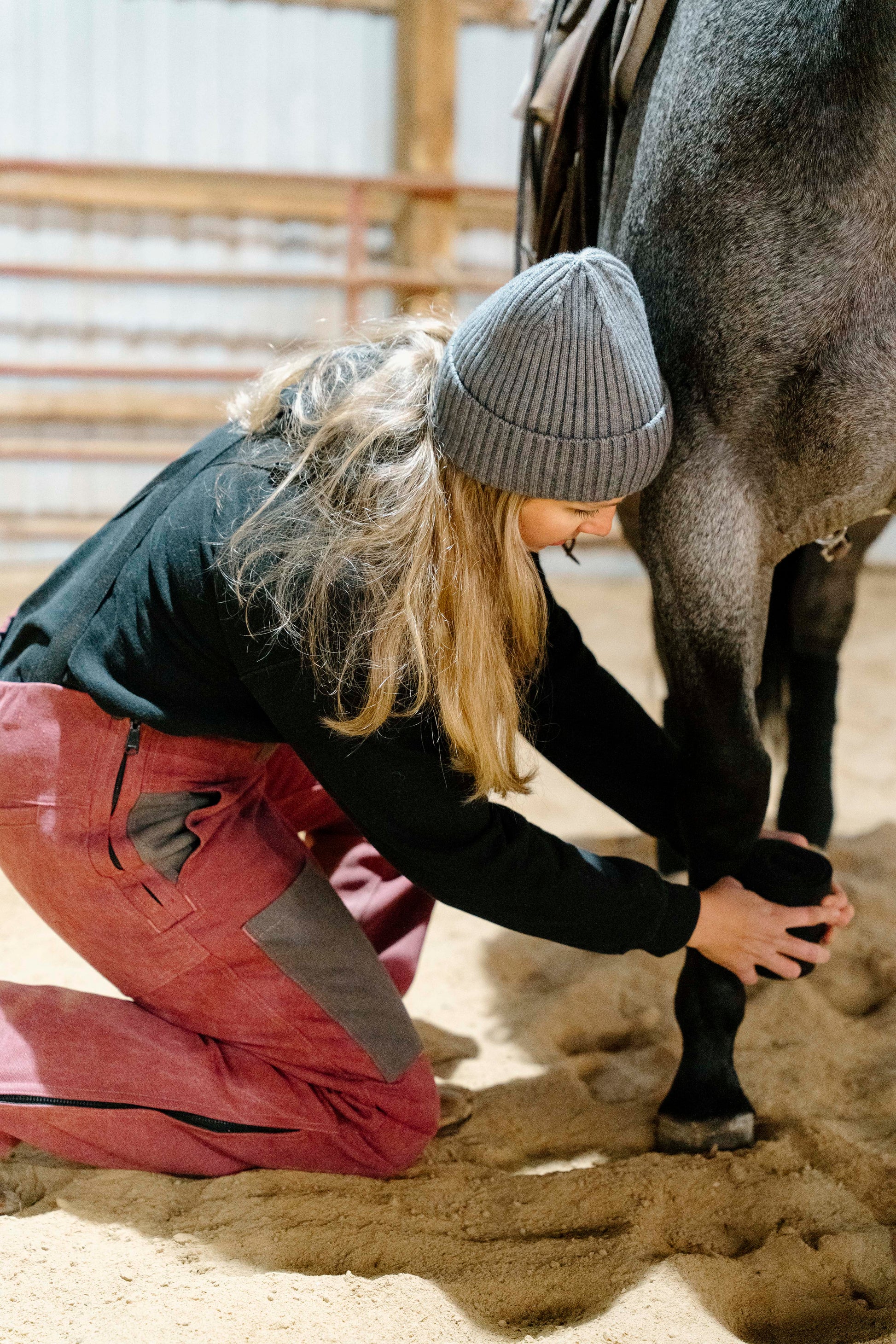 Person kneeling down to check a horse's foot in an indoor arena
