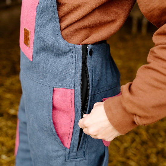Person wearing a blue overalls with pink pockets in an outdoor setting