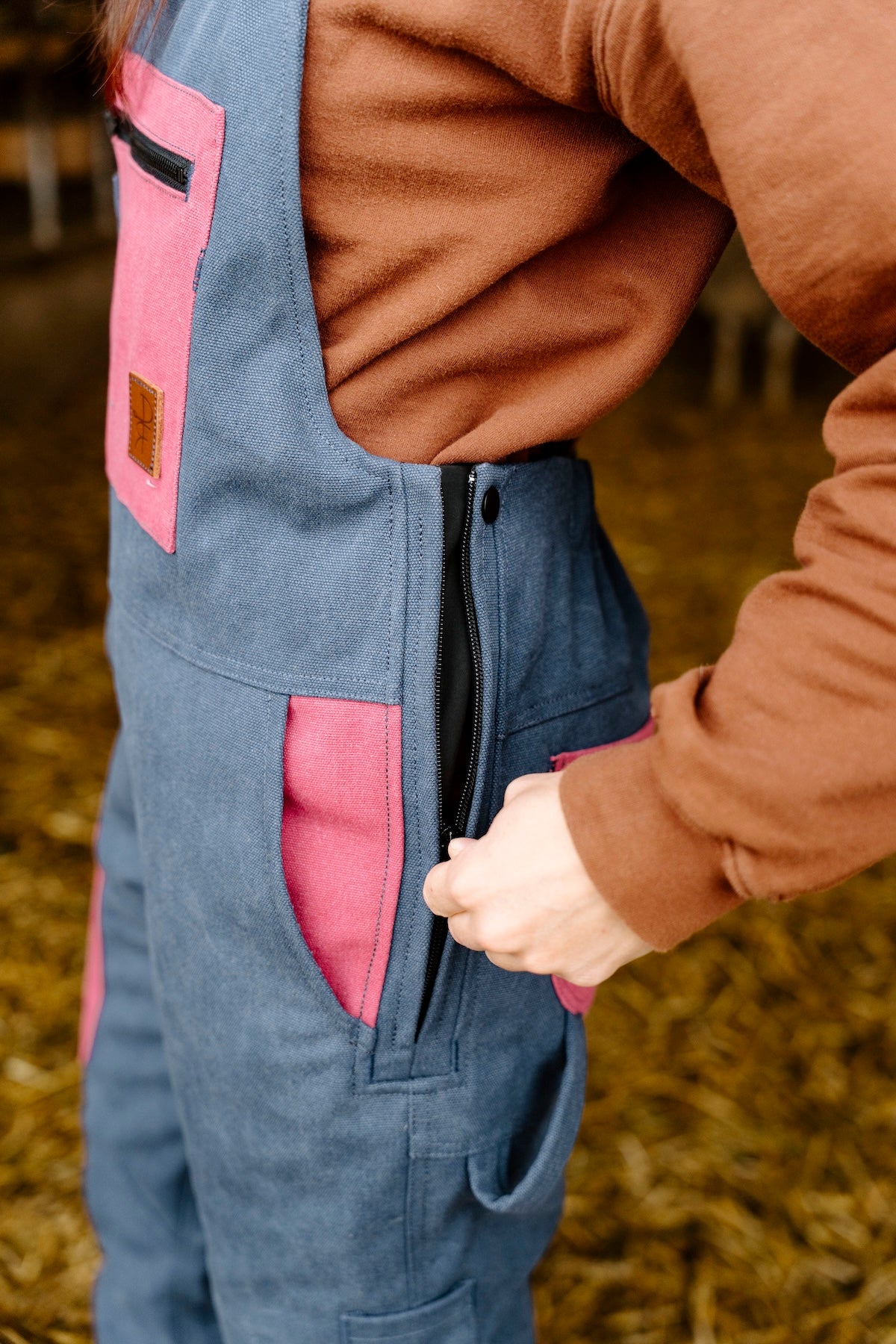 Person wearing a blue overalls with pink pockets in an outdoor setting
