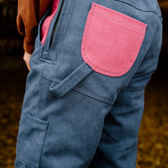 Blue overalls with a pink pocket worn by a person, standing on a grassy field.