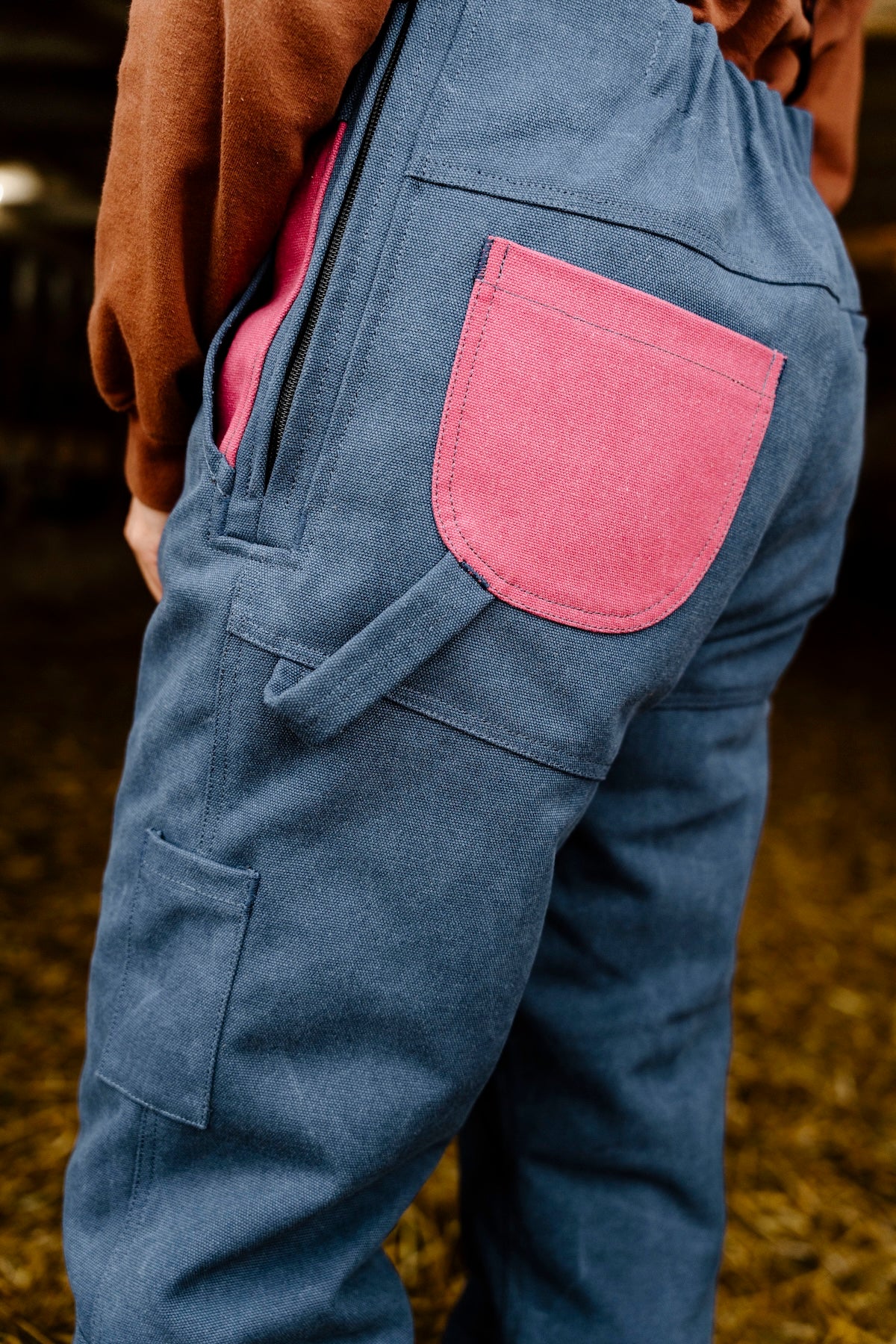Blue overalls with a pink pocket worn by a person, standing on a grassy field.