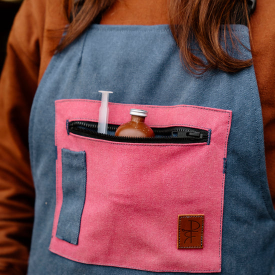 Person wearing a blue overalls with pink pocket and various items inside.