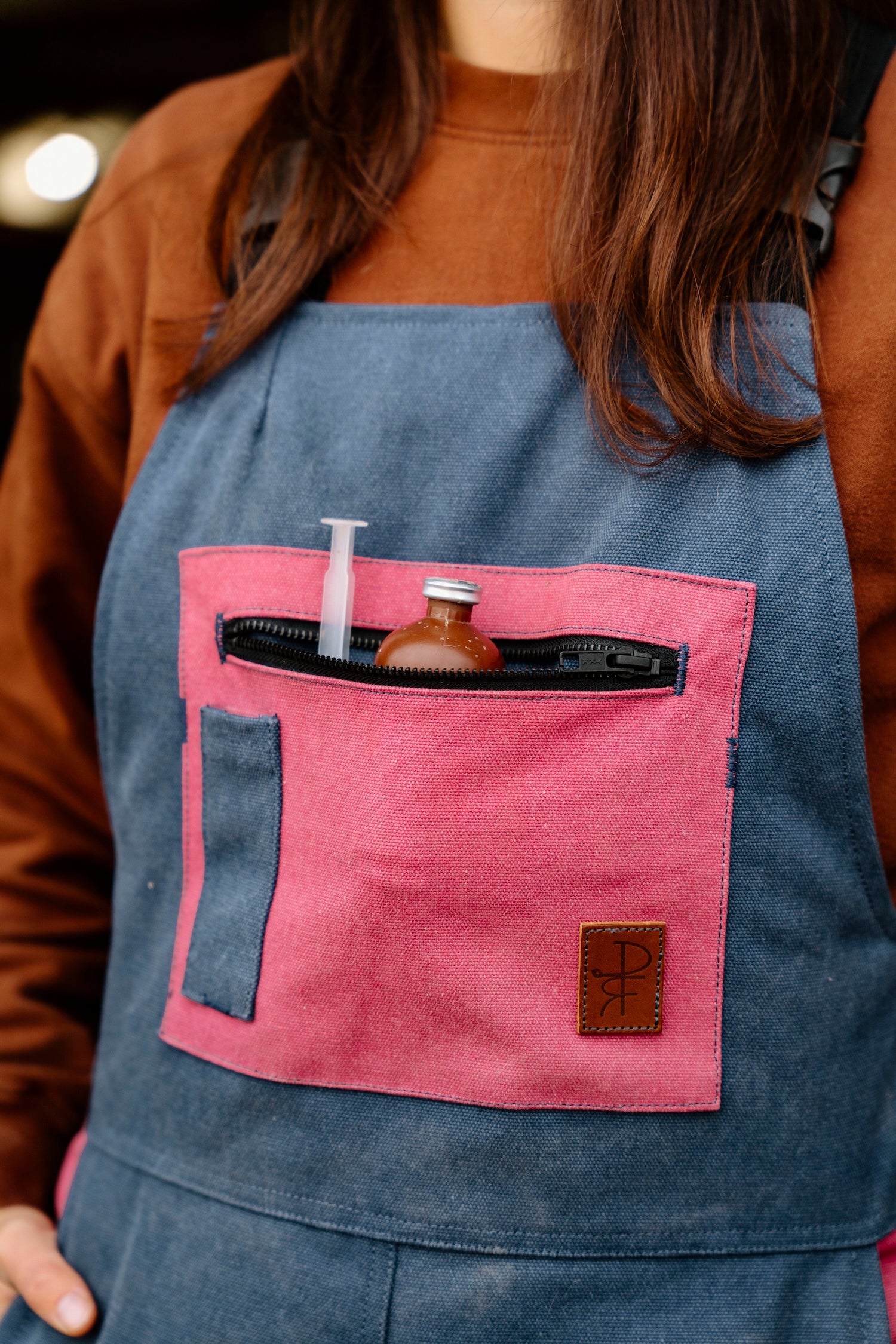 Person wearing a blue overalls with pink pocket and various items inside.