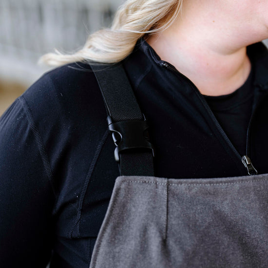 Person wearing dark shirt with grey overalls on displaying buckles 