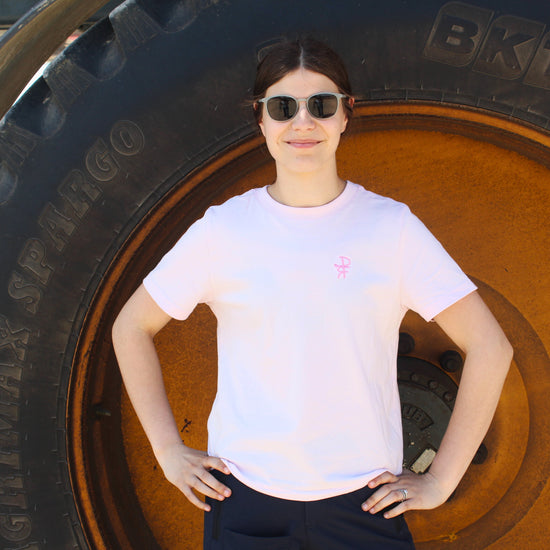 Person standing in front of a large tire wearing sunglasses and a pink t-shirt.