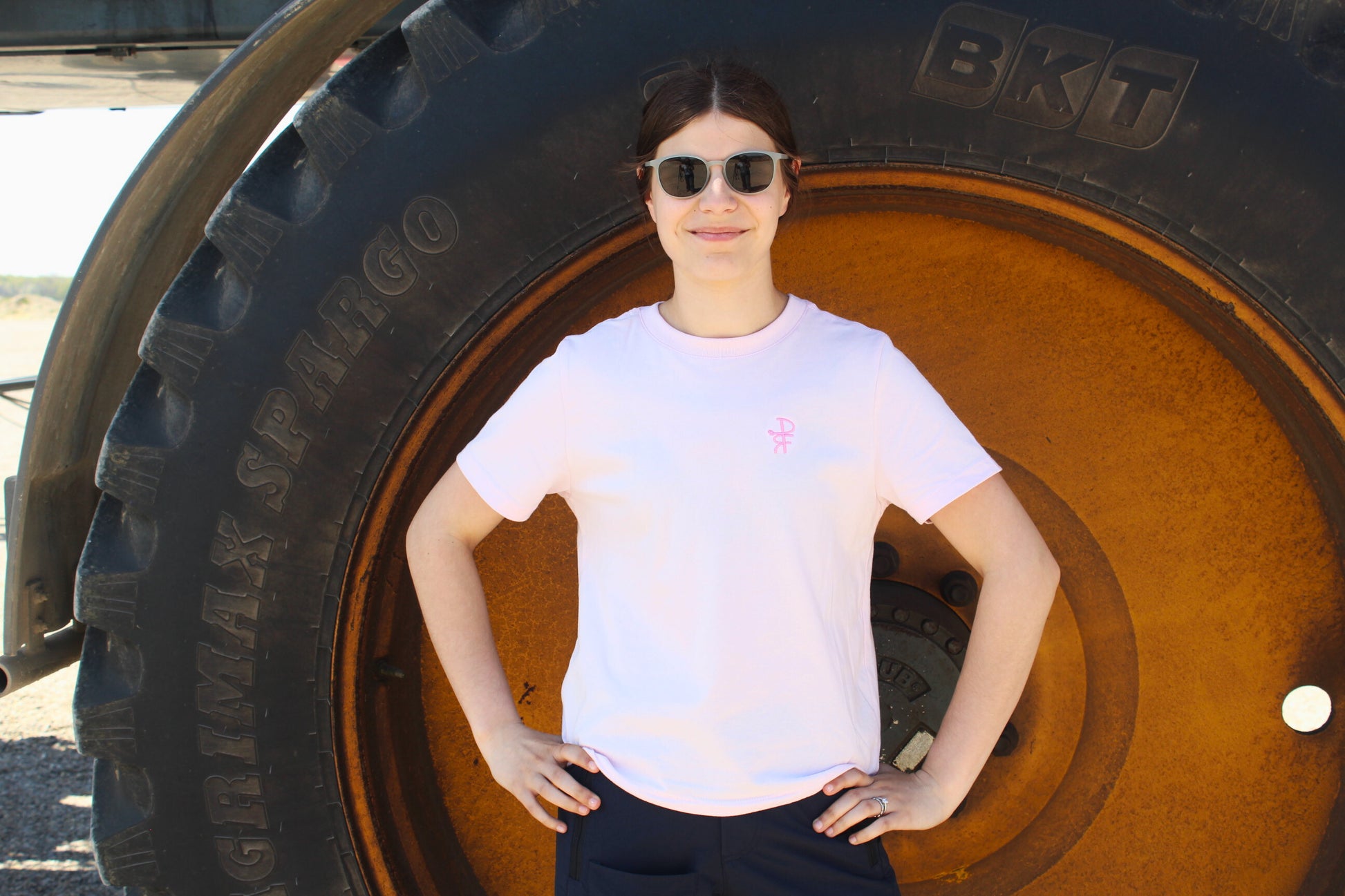 Person standing in front of a large tire wearing sunglasses and a pink t-shirt.