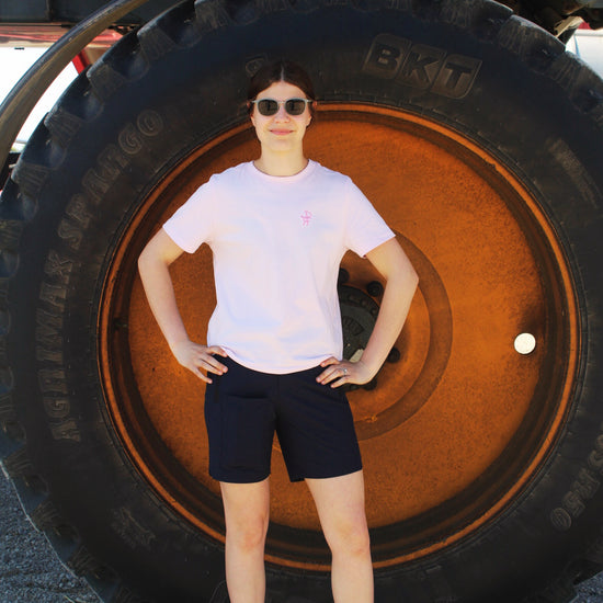 Person standing in front of a large tire, wearing a pink shirt and black shorts.