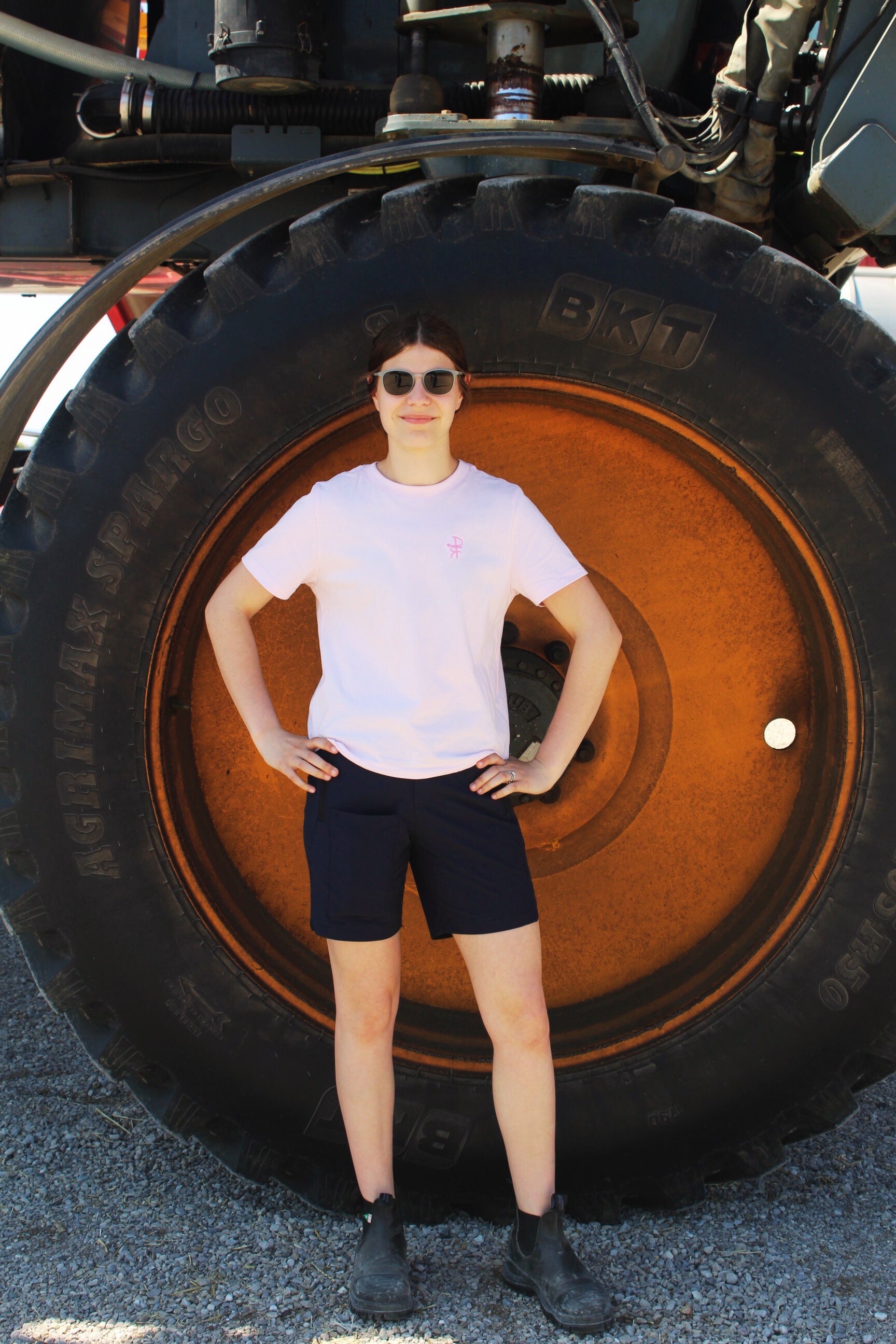 Person standing in front of a large tire, wearing a pink shirt and black shorts.