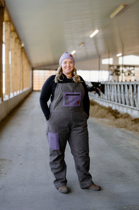 A person wearing a purple and gray insulated overall, standing in a barn setting.