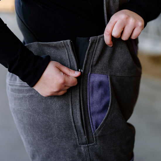 Person un-zipping grey overalls with purple pockets 