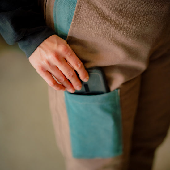 Person wearing brown and turquoise overalls putting object into pocket 