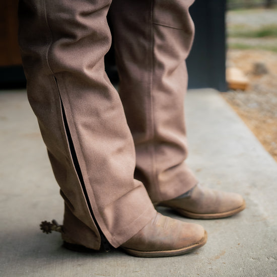 Person wearing brown overalls with zipper leg and cowboy boots
