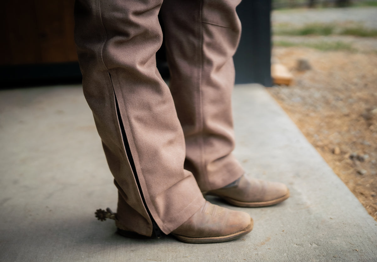 Person wearing brown overalls with zipper leg and cowboy boots
