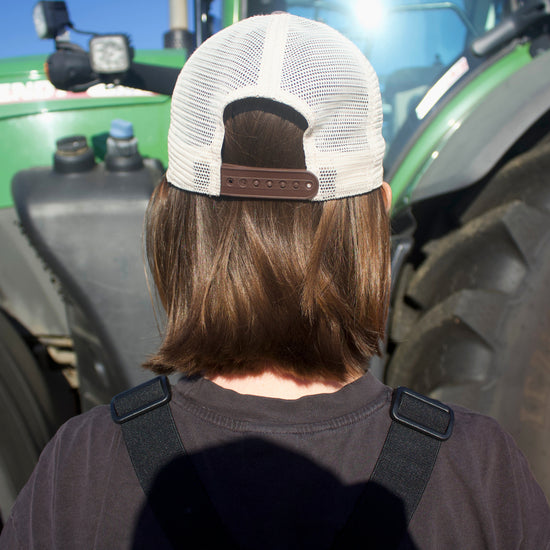 Person wearing a cap and overalls standing in front of a large green tractor.