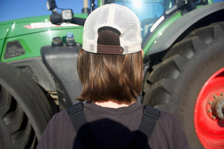 Person wearing a cap and overalls standing in front of a large green tractor.