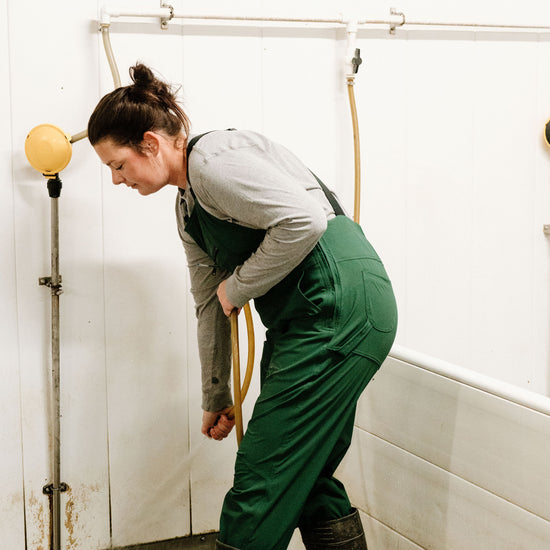 Lady using hose in green overalls and rubber boots